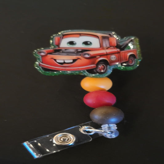 It's our favorite tow truck Mater. This iconic badge reel tow truck will be sure to pull you through the day. A shiny glitter base and is finished with 3 color coordinated silicone beads.