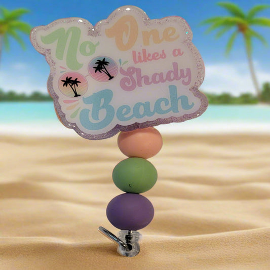 Ahhh the beach life. Here we have our acrylic badge reel stating No One Likes a Shady Beach. But what if we were located on a beach???? Quite the Paradox. This badge reel has a light purple glitter back and 3 silicone color coordinated beads to finish the look.