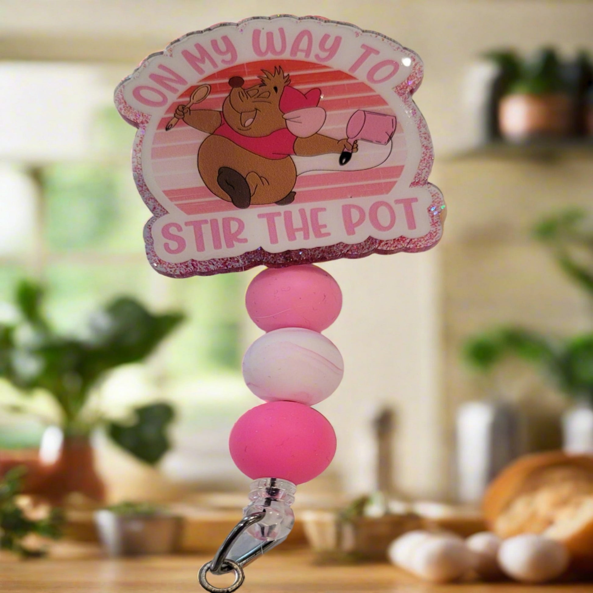 Well this could go 1 of 2 ways. Either heading to the kitchen to Stir The Pot or your on the way to cause some trouble and Stir the Pot that way. Either way this cute acrylic badge reel features a pink glitter back and 3 color coordinated silicone beads.