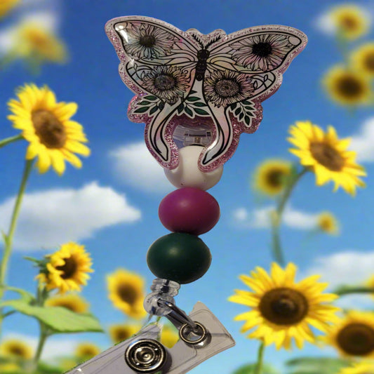 This Badge Reel features a beautiful moth with sunflower images on each wing and a shiny purple glitter background. The colorful moth is complemented by three color-coordinated silicone beads for an extra touch of charm. Sure to be a hit with any animal lover.