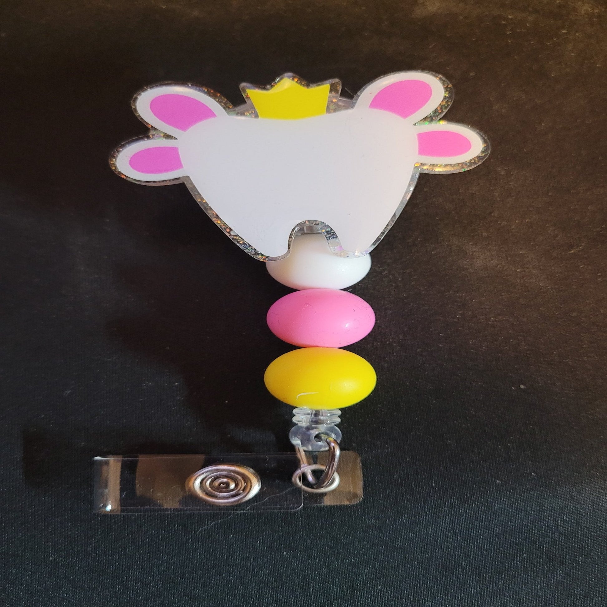 Part of our latest collection of Medical Badge Reels available now, The Tooth Fairy is arriving. Featuring a white shiny tooth, cute little wings, gold crown and a glitter base adorned with coordinating beads. Somebody is getting a quarter under their pillow tonight!