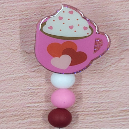 New to our Badge Reel lineup is our Mug of Love. This Valentine Cocoa is sure to warm anybody's heart with a pink mug full of cocoa and topped with whipped cream and sprinkles. Featuring a glitter base with coordinated beads, this is the perfect accessory for the holiday season.