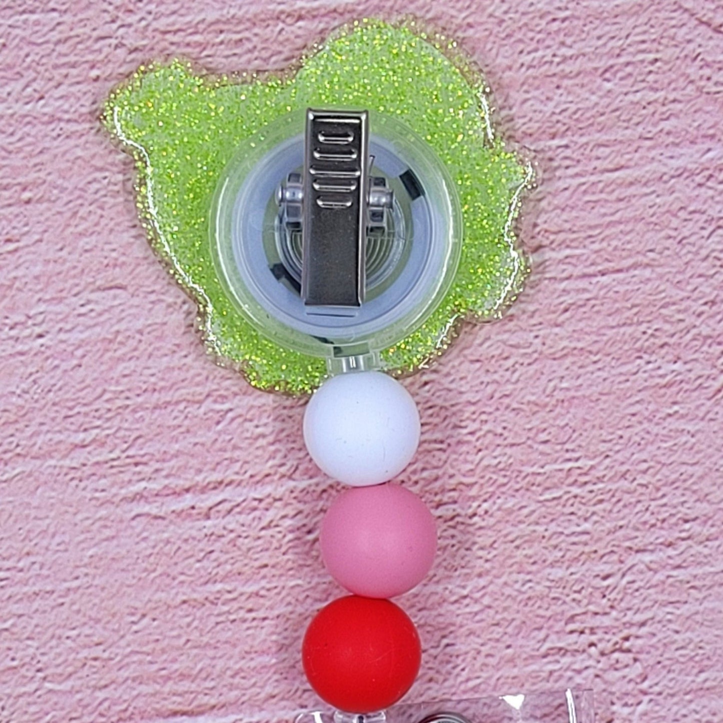 The Badge Reel Valentine Love Hound features Snoopy, the lovable pooch, ready for Valentine's day. Cool shades and hearts are highlighted on a green glitter base with matching beads in the background