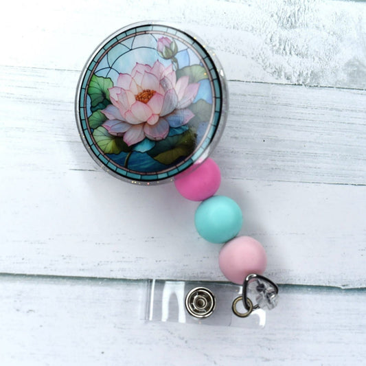 This acrylic water lily badge reel is designed with stained glass and features teal and two distinct shades of pink silicone accent beads.