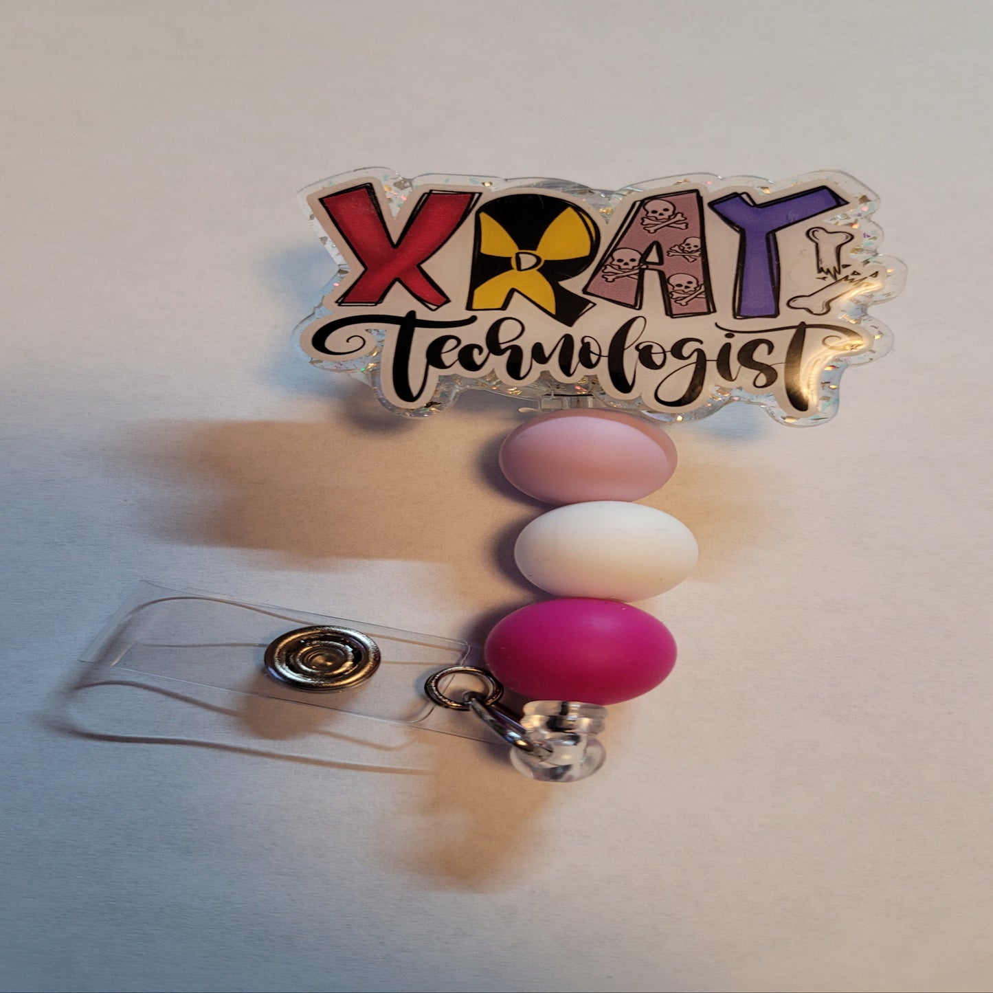 Introducing our latest addition to the Medical Field Collection - the vibrant and lively XRay Technologist Badge Reel! Its clear chunky glitter back brings some sparkly fun to your workday, and the 3 matching silicone beads add the perfect touch of color.