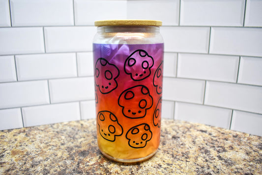 Happy Mushrooms with a beautiful orange to purple gradient background on a Pink Shimmer frosted 16 oz glass can tumbler with straw and lid. 