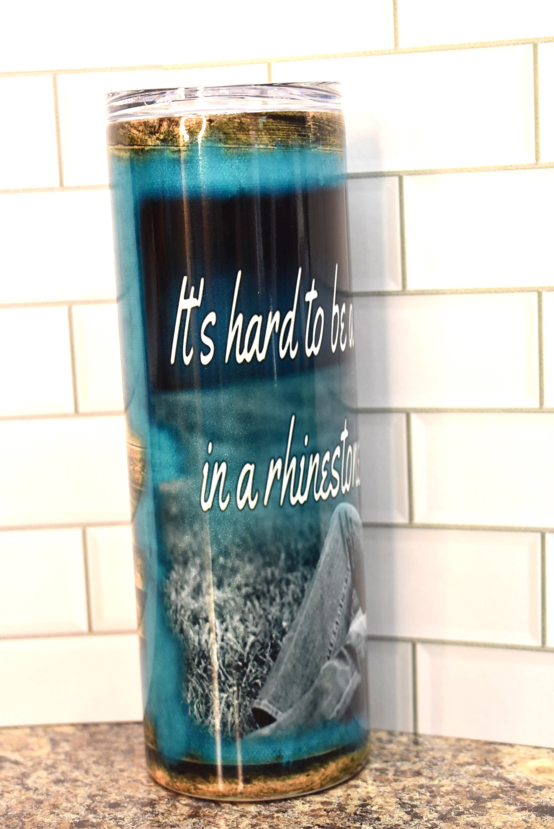 This 20 oz stainless steel Makerflo tumbler features the 1 and only Dolly Parton as she plays a guitar with the phrase....It's hard to be a Diamond in a Rhinestone World .