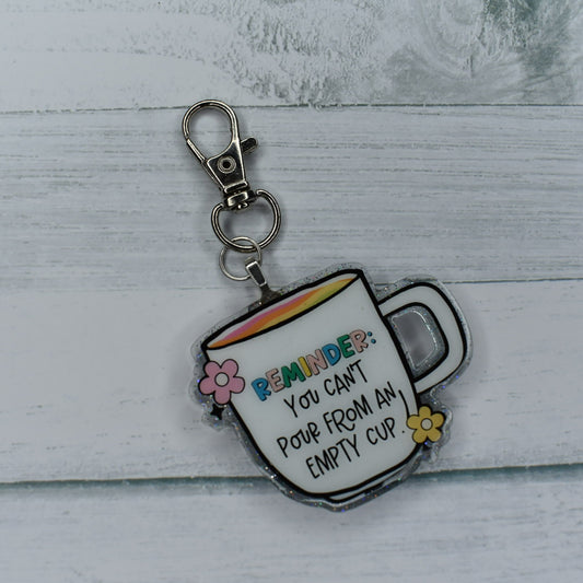 Reminder: You Can't Pour From An Empty Cup. This Bag Tag is a simple reminder that we need to take care of ourselves as we take care of others. A silver grey glitter background in the shape of a coffee cup with that phrase on the from. A pink & yellow flower finish the look on this hand crafted acrylic resin bag tag.