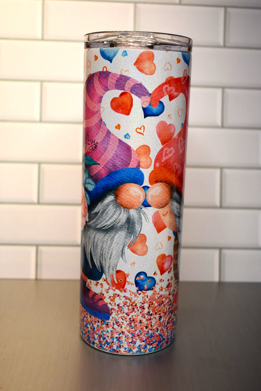 This 20 oz tumbler features a Gnome Love Couple Nose To Nose standing in confetti and floating hearts around them.