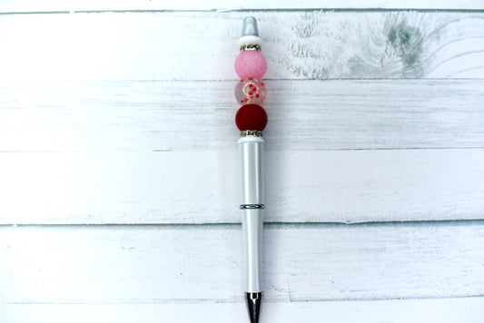 This pen will steal your heart. A white base with a pink & red accent bead flank a clear silicone bead with tiny hearts inside. Sparkling gem rings hold it all together. 1 extra black ink refill included.