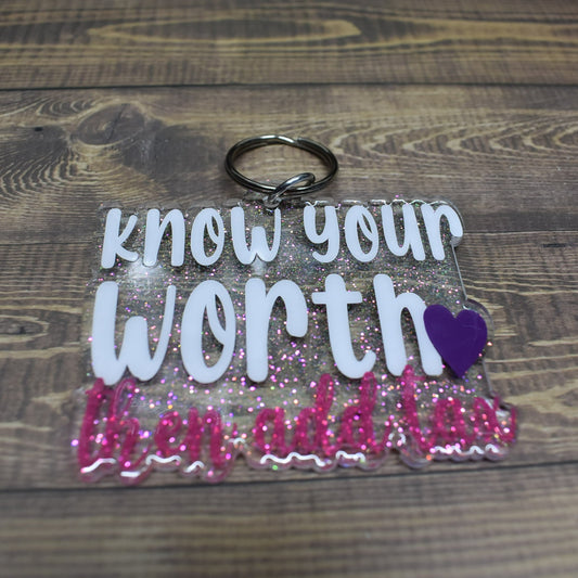 A glossy acrylic keychain, made atop a clear resin base, displays white and pink lettering that reads "Know Your Worth Then Add Tax".