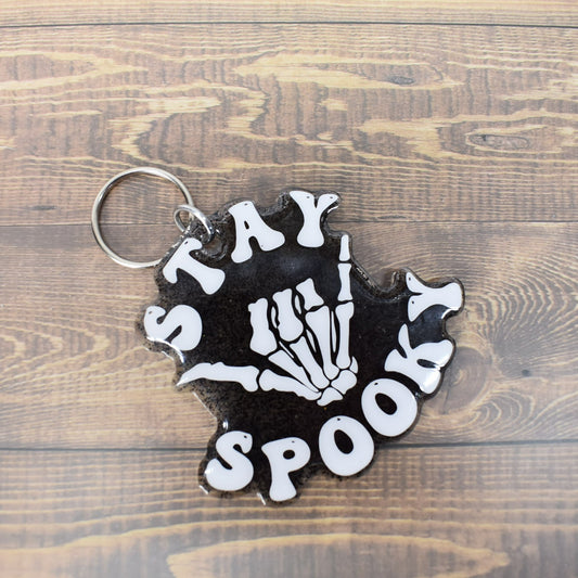 Acrylic keychain starts with a clear resin base with black glitter mixed in topped off with a  skeleton hand saying Stay Spooky