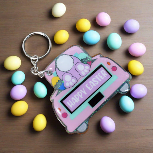 Crafted from acrylic, this keychain features an image of the Easter Bunny climbing in the trunk of a car while searching for Easter eggs, with cheerful 'Happy Easter' plates.