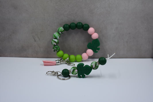 This silicone bead wristlet features a Monstera plant focal bead, faux leather tassel, and a matching straight-pattern keychain.